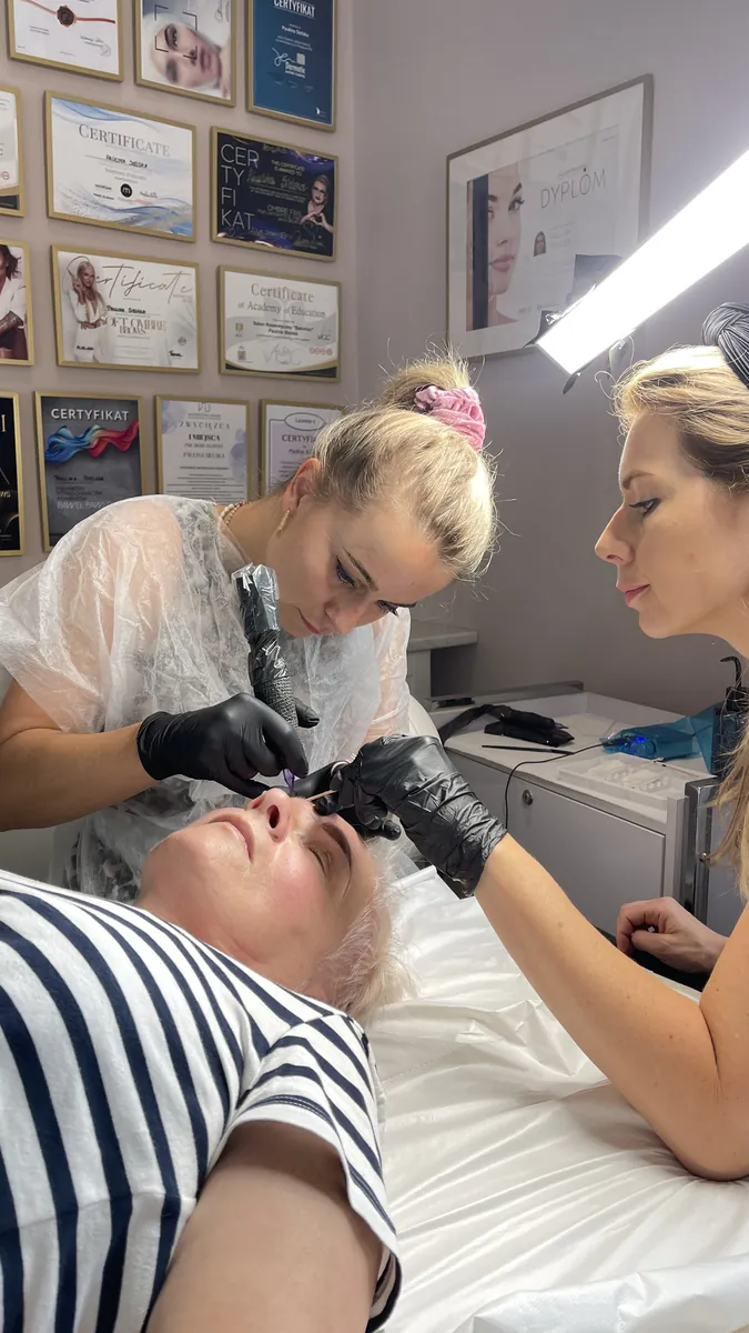 Paulina Sielska nadzoruje kursantkę podczas pigmentacji brwi, w tle certyfikaty